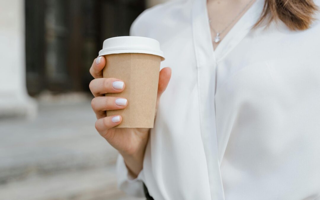 Woman in a white blouse holding a coffee in a paper takeaway cup